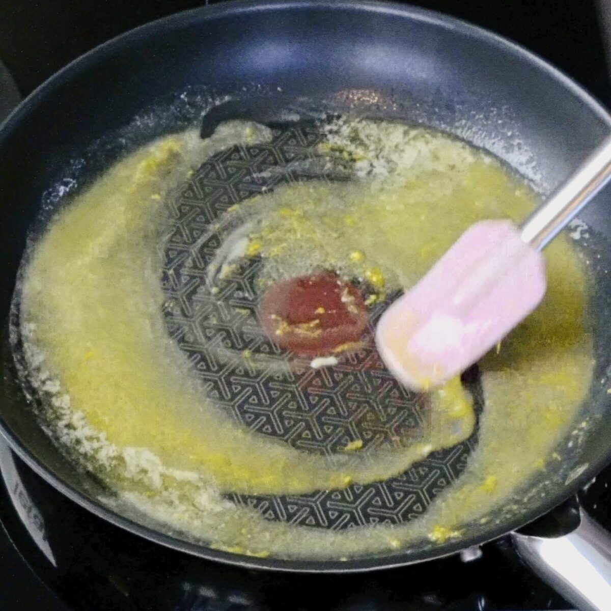 A person stirring lemon zest into melted butter with a spatula.