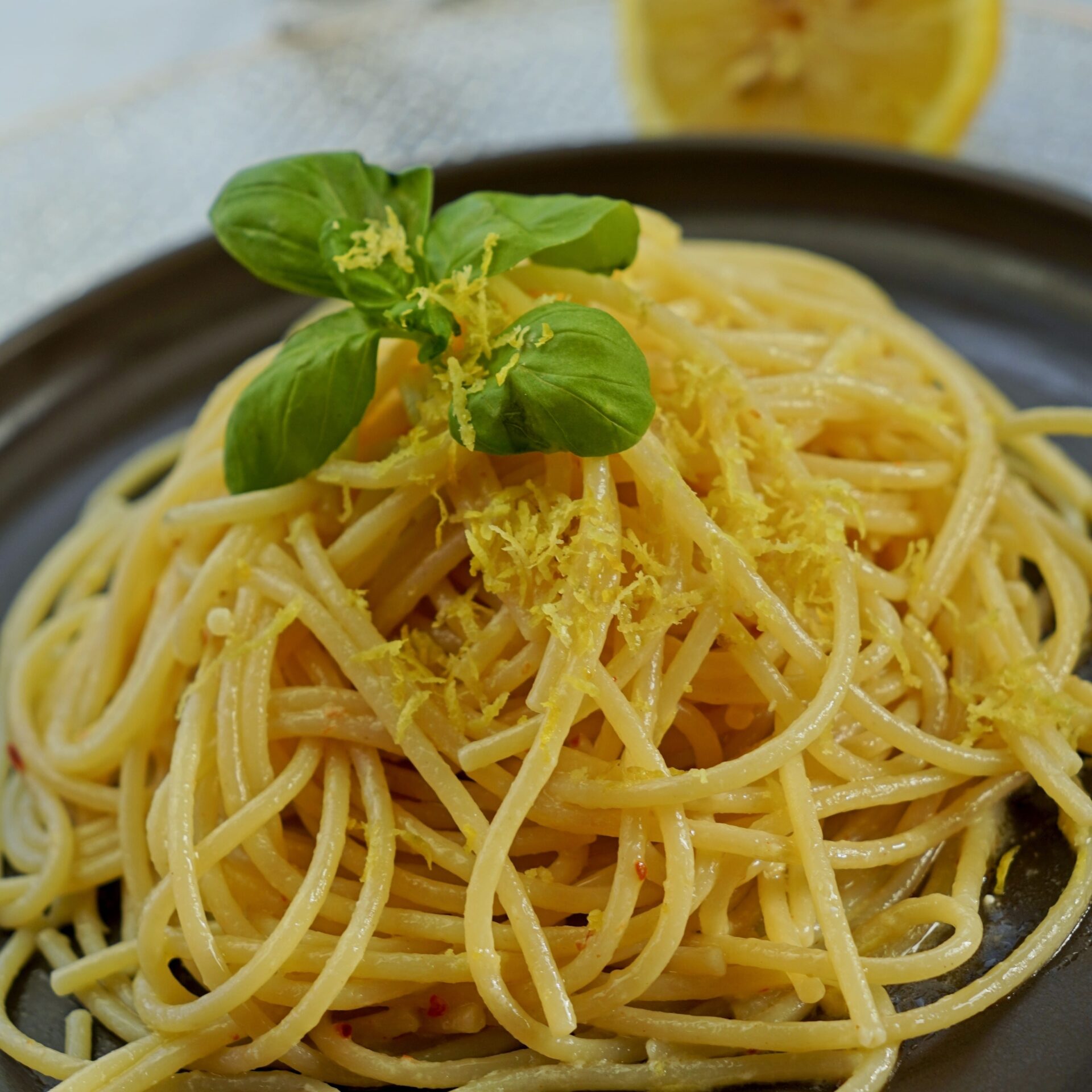 Close-up of freshly cooked lemon butter pasta with lemon zest and basil leaves.