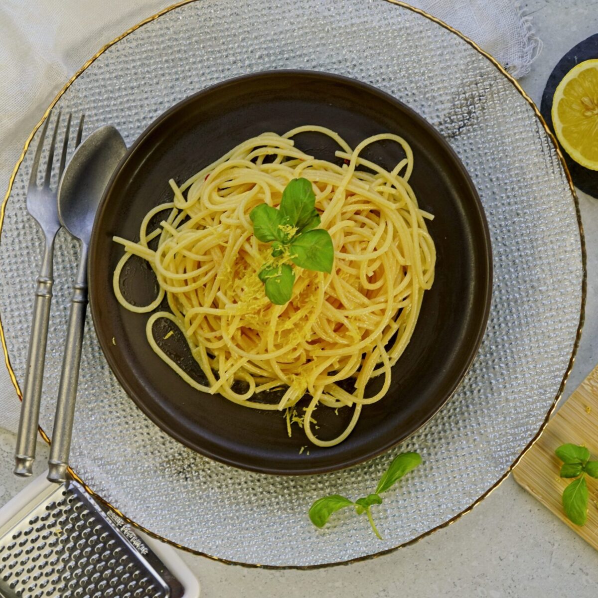Top-down view of lemon butter pasta garnished with basil leaves, with a lemon half on the side.