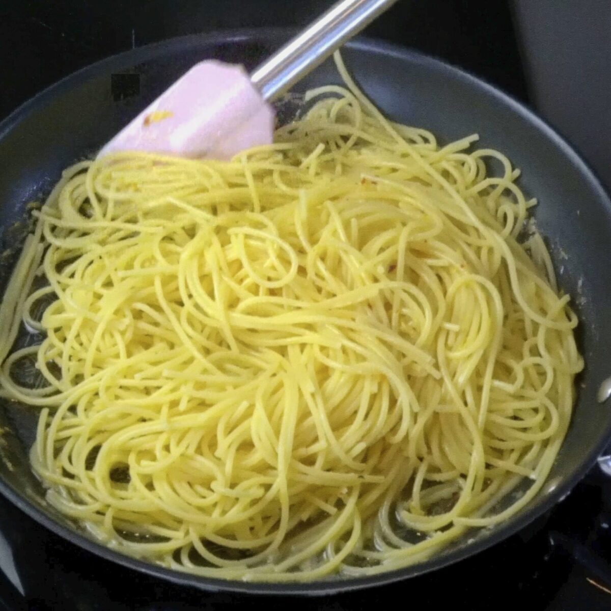 Mixing pasta with lemon butter sauce in a pan.