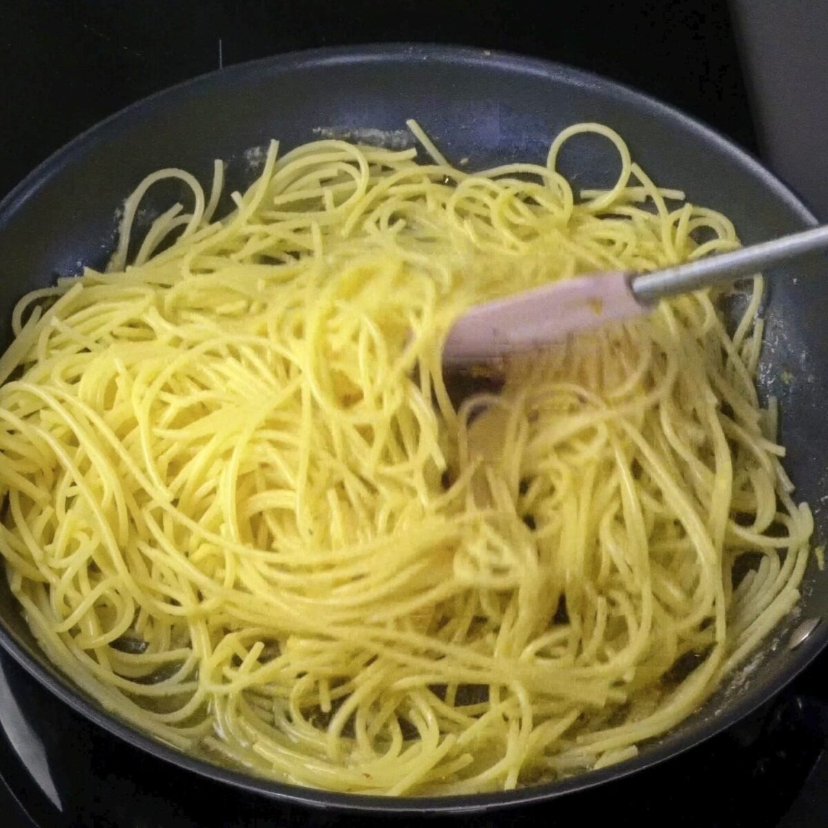 Mixing pasta with lemon butter sauce and freshly added lemon juice in a pan.