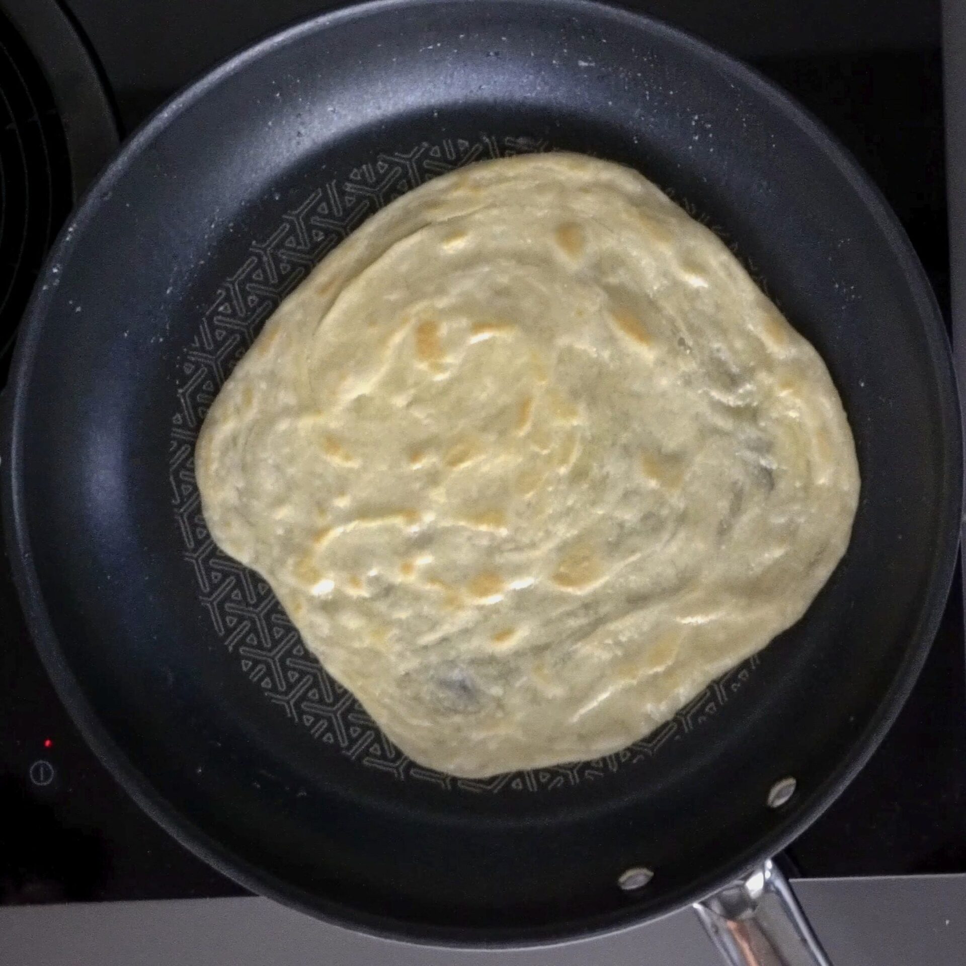 Light brown spots forming on the roti as it cooks.