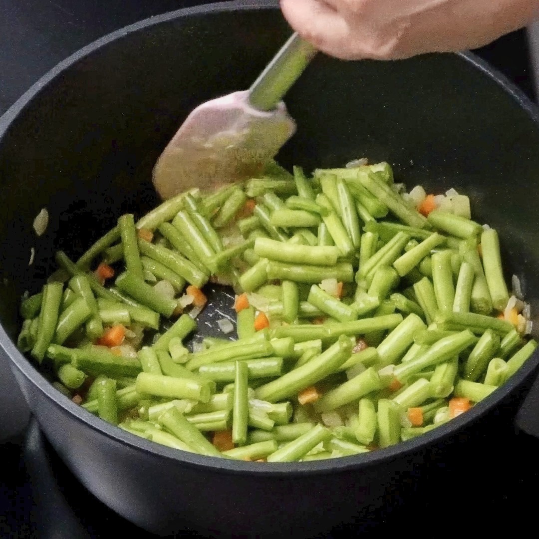 Mixing green beans with other vegetables in the pot.