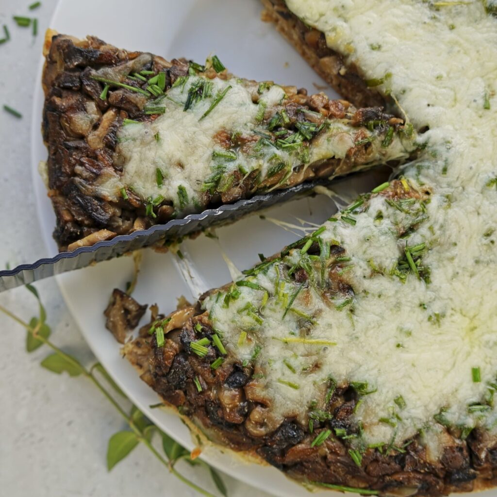 A person slices into a mushroom pie, revealing melted cheese oozing between the pieces.