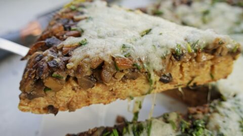 A person is holding a piece of mushroom pie, loaded with mushrooms with melted cheese on top.