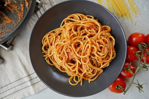 A grey plate with a lot of red sauce and spaghetti from above. On the right side there are fresh tomatoes and on the left a pan with more sauce.