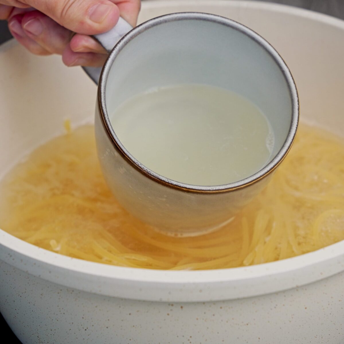 Scooping out starchy pasta water during pasta cooking.