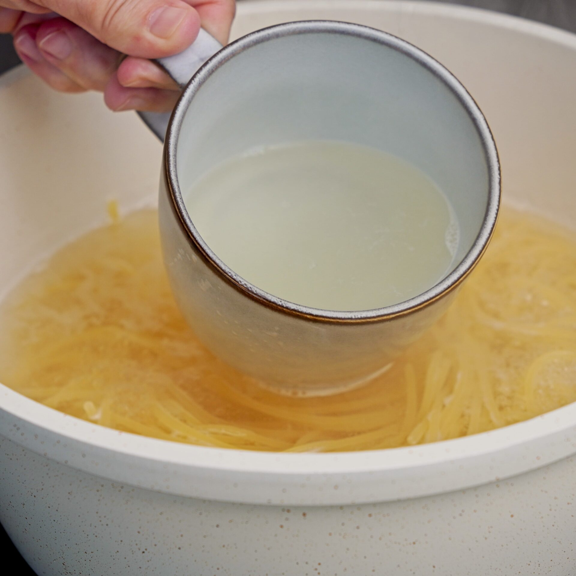 Scooping out starchy pasta water during pasta cooking.