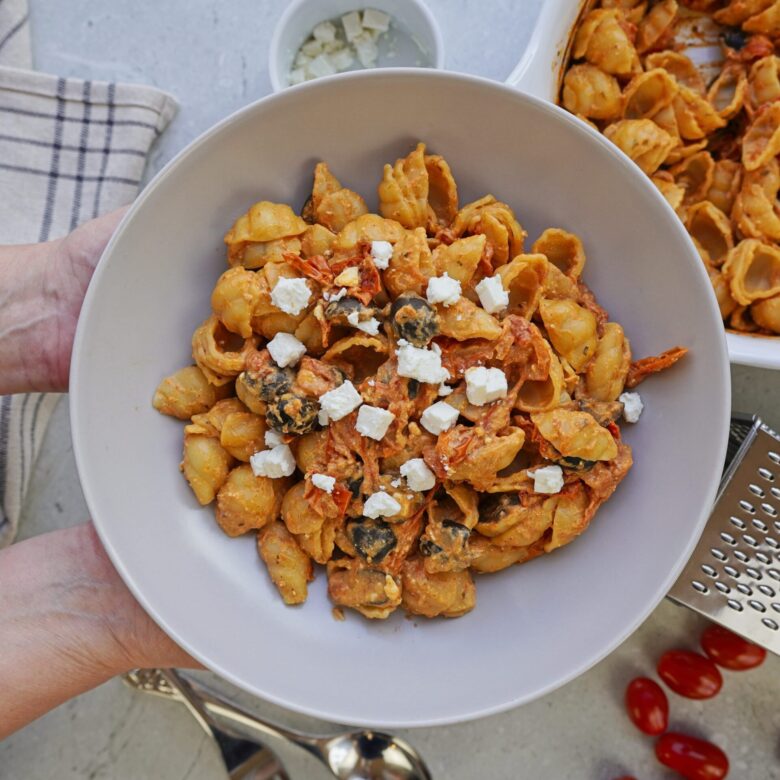 Person holding a plate of creamy pasta topped with feta cheese.