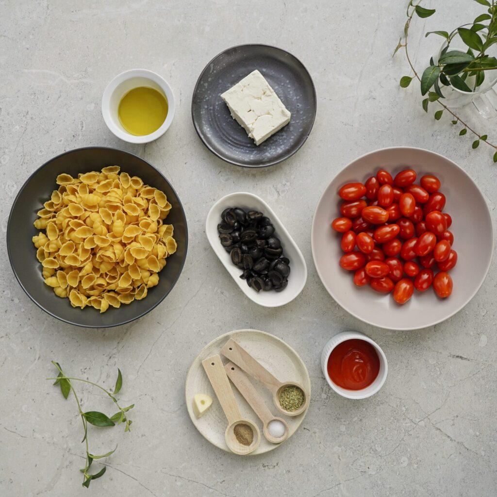 Ingredients for pasta with cherry tomatoes: pasta, tomatoes, olives, passata, feta, olive oil, and spices on a separate plate.