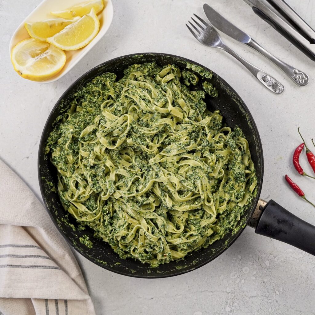 A pan with creamy pasta ready to be eaten. To add some freshness there are lemon slices above the pan. 