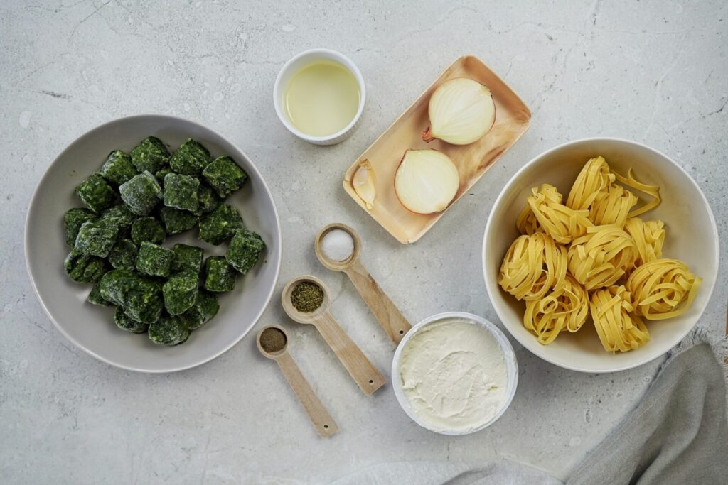 Ingredients for tagliatelle pasta with spinach and ricotta including tagliatelle pasta, frozen spinach, ricotta, oil, onions, garlic, pasta water, oregano, black pepper, and salt.