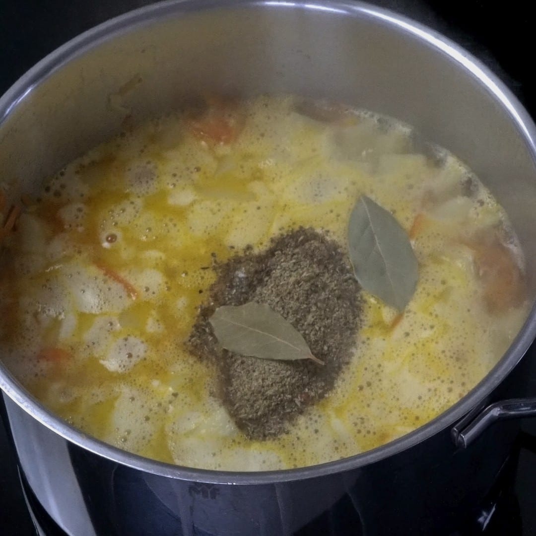 Adding spices and bay leaves to the pot with potatoes.