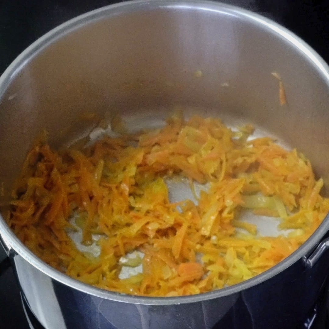 Sautéing carrots and onions in a pot for cheesy potato soup.