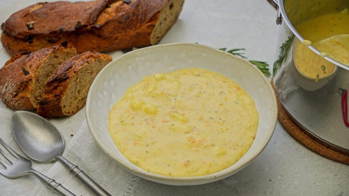 Creamy cheddar potato soup in a bowl with a few pieces of bread on the side.