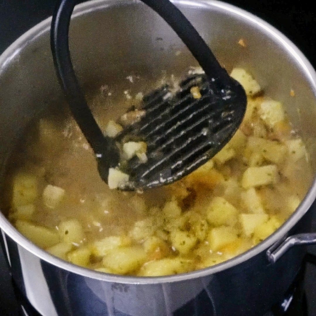 Mashing potatoes with a potato masher to thicken the soup.