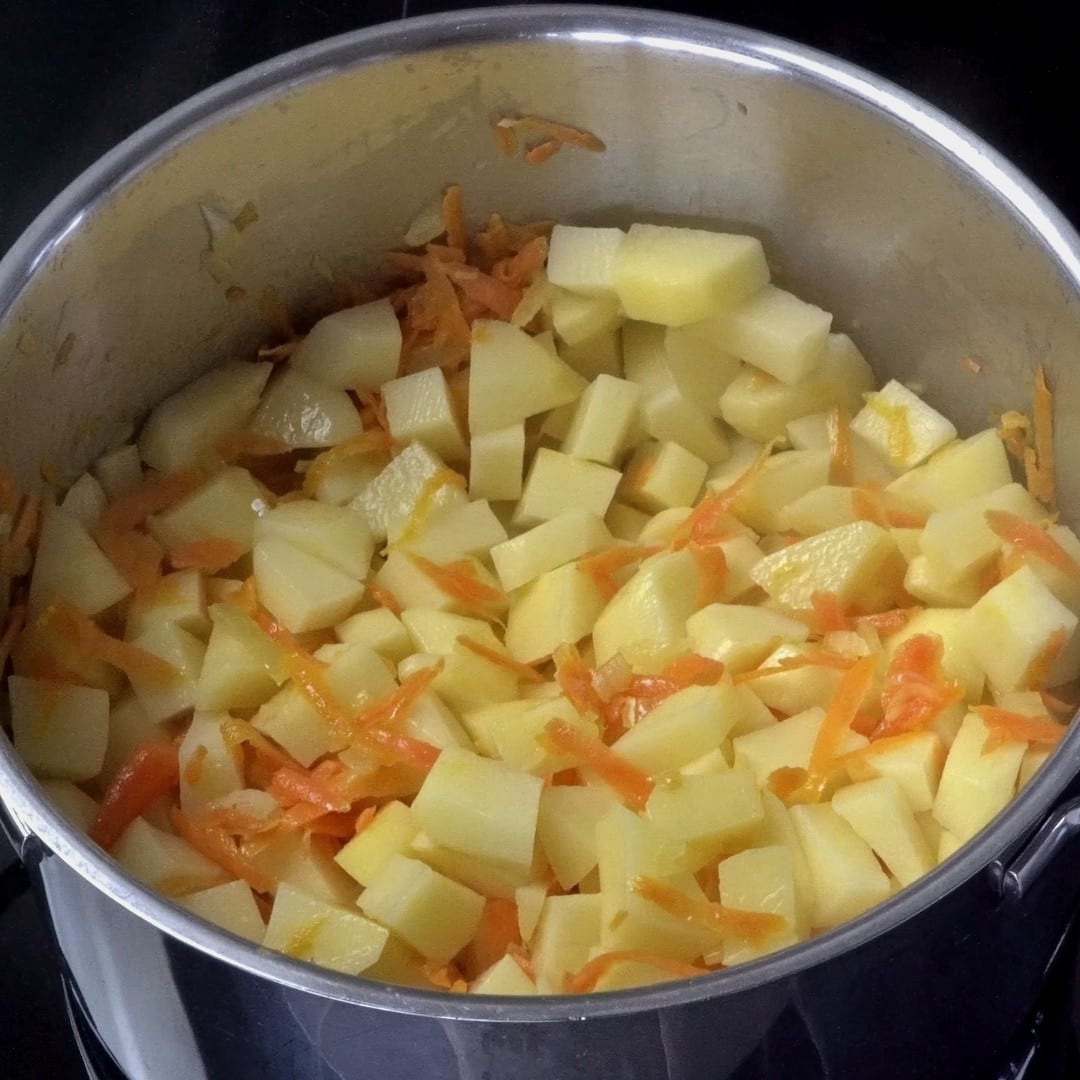 Mixing potatoes, grated carrots, and onions in a pot.