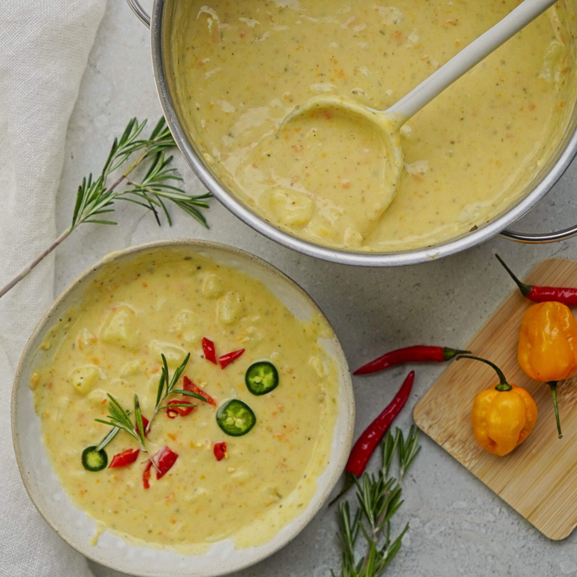 Potato cheese soup in a pot with a ladle full of soup above it and a bowl of creamy soup nearby.