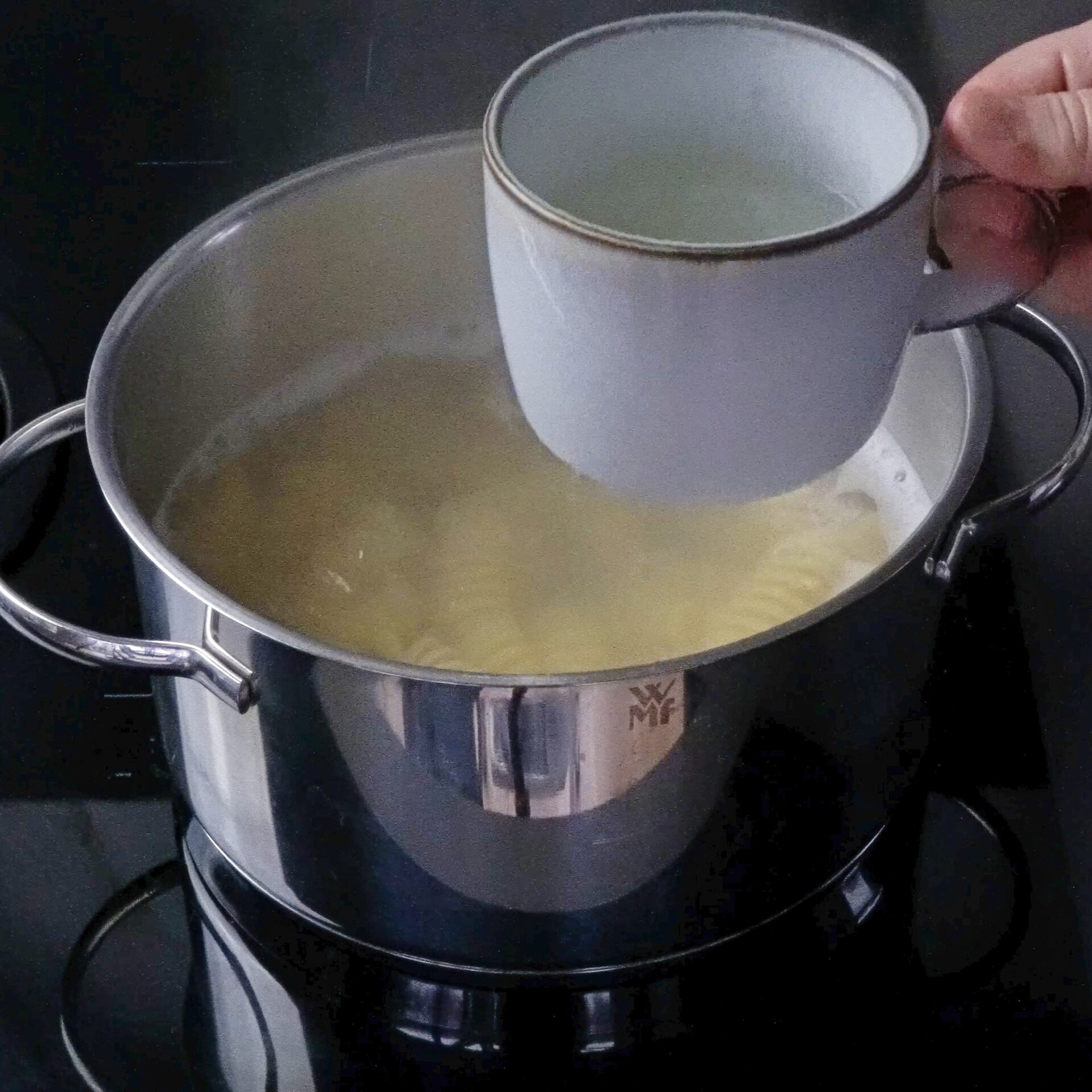 Scooping pasta water from the pot before draining the pasta.