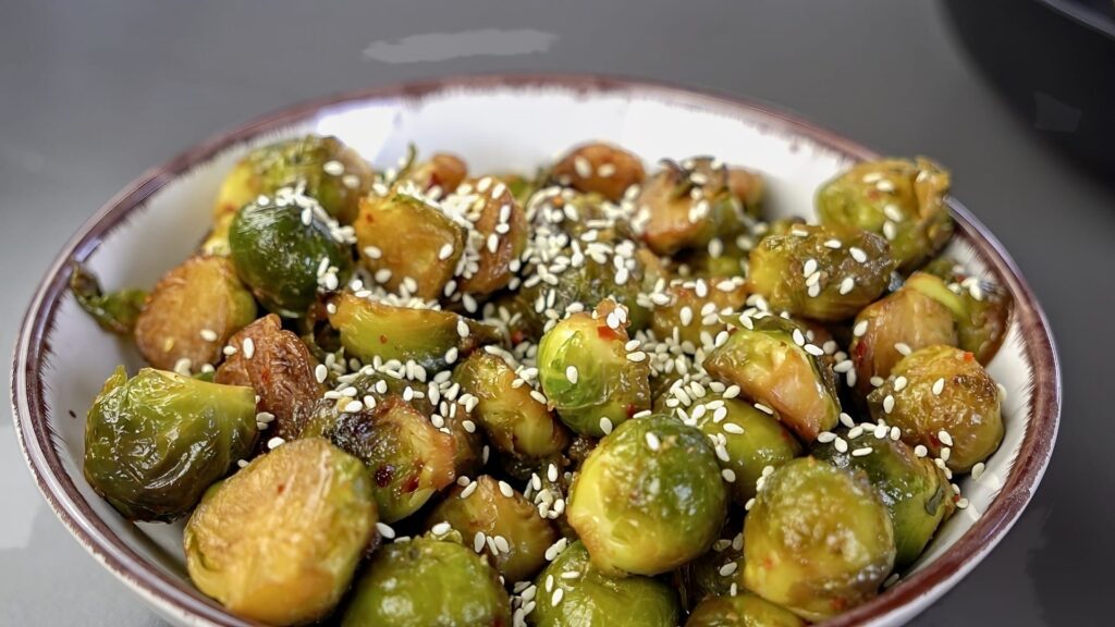 Adding sesame seeds to a bowl with Brussels sprouts.