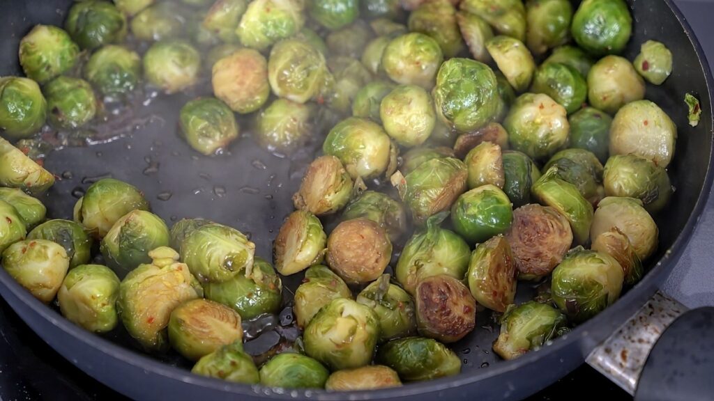 Simmering Brussels sprouts in a pan with soy sauce and rice vinegar.