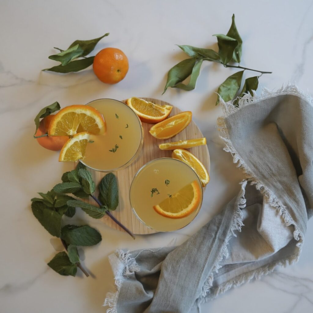 On a table stand glasses with fresh orange juice. Orange halves are lying on a table. Near them there are small oranges with leaves.