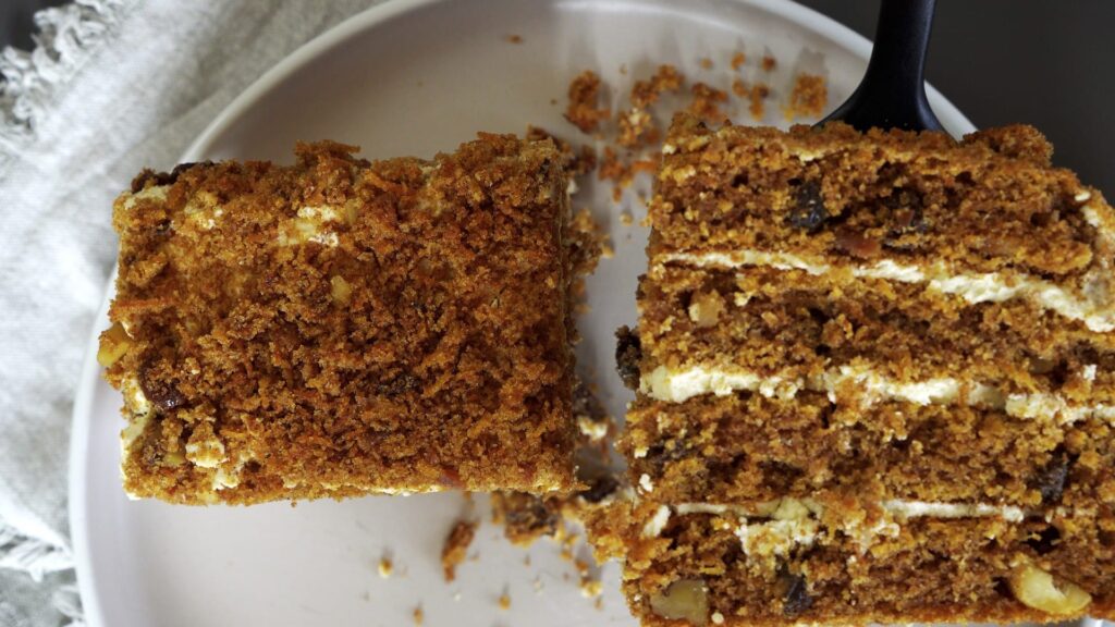 Wrapping carrot cake with cream cheese frosting in plastic wrap for storage.