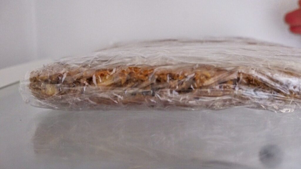 Placing carrot cake layers wrapped in plastic wrap in the fridge.