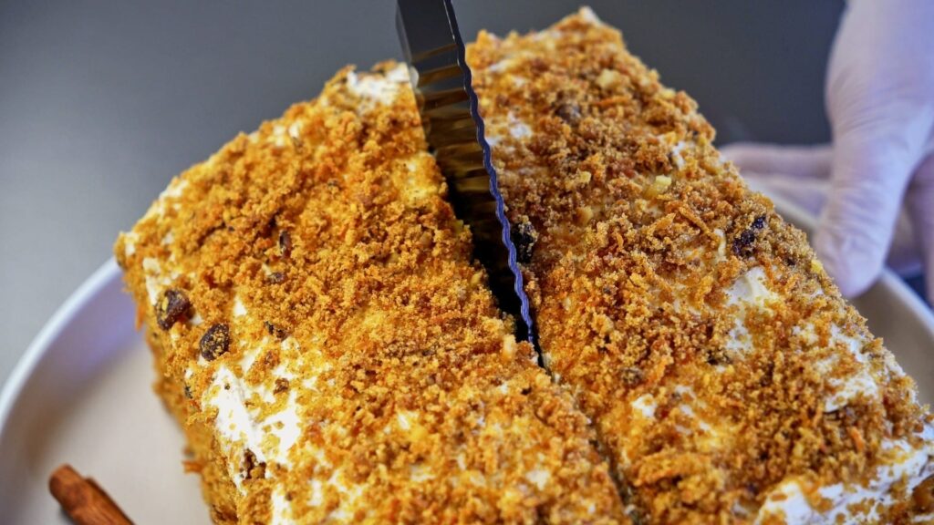 Slicing extra soft carrot cake with cream cheese frosting.