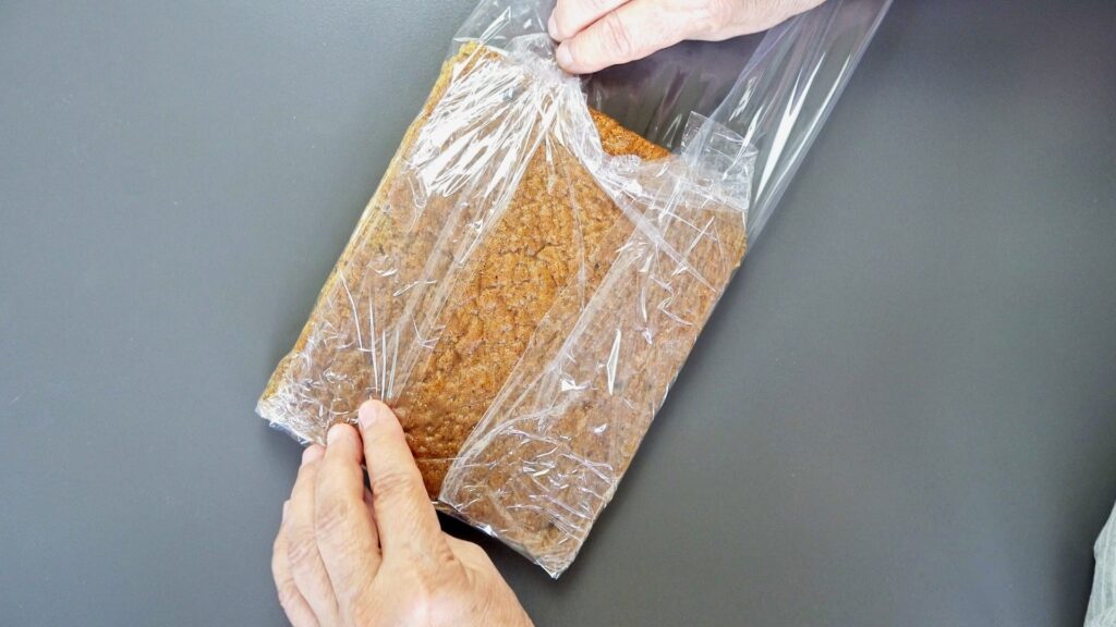 Wrapping carrot cake layers in plastic wrap before storage.