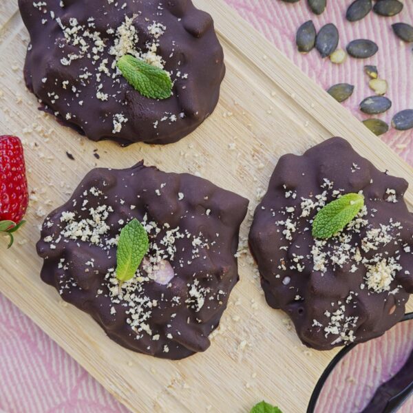 Chocolate-covered strawberry clusters with mint leaves on a board.