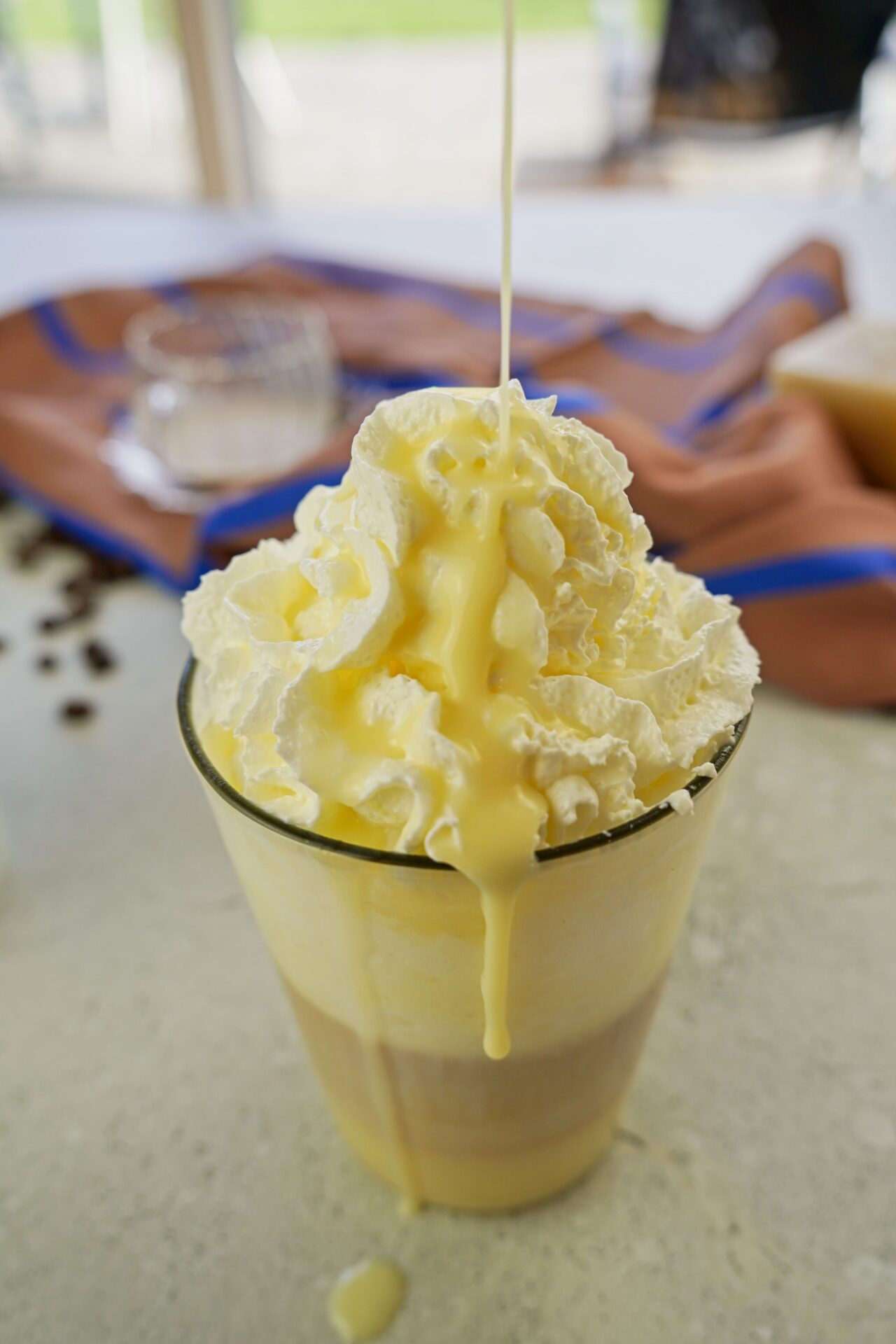 Pouring white chocolate syrup over a cup of latte topped with whipped cream.