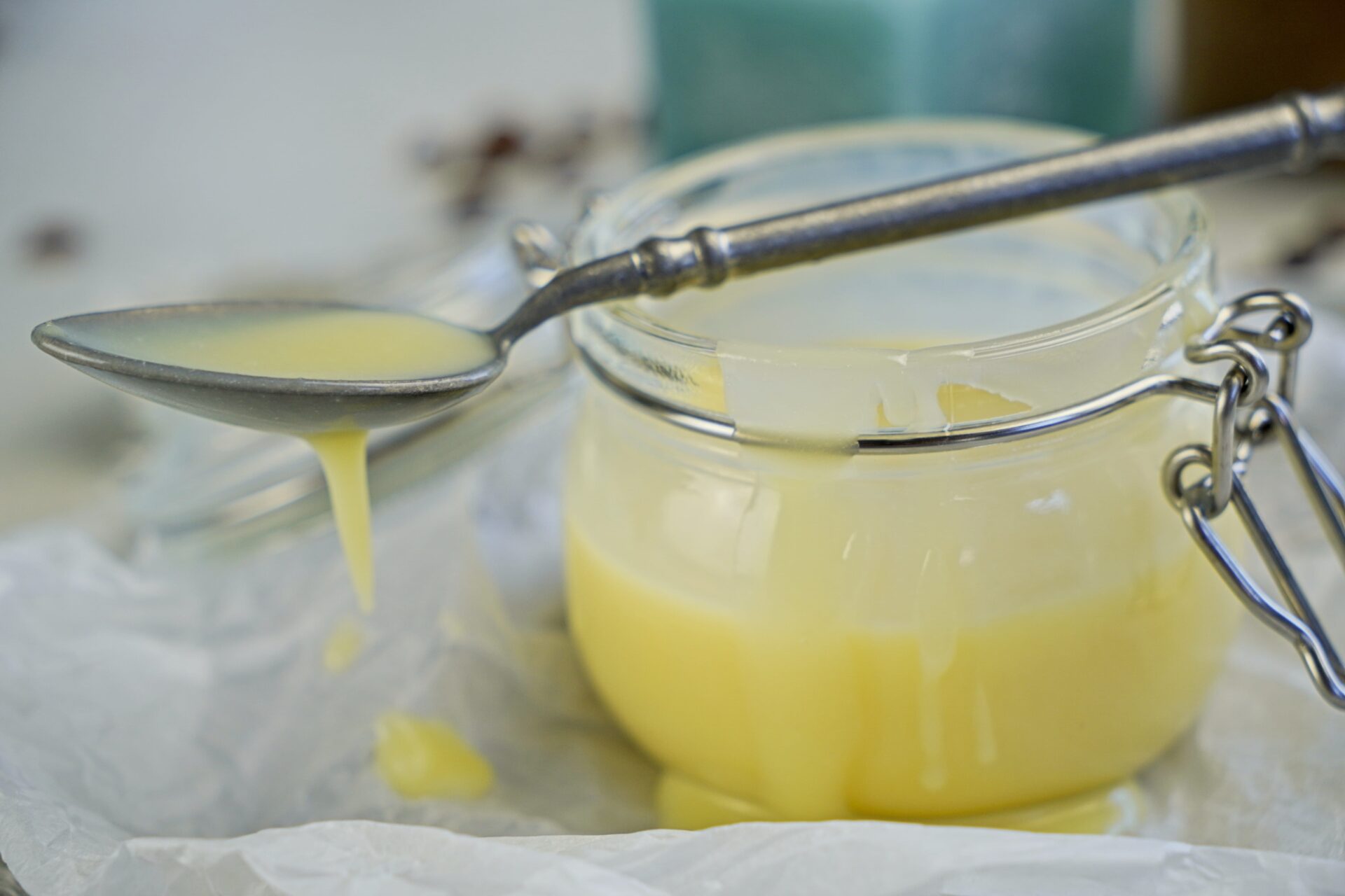 A spoon with white chocolate coffee syrup resting on top of a glass jar filled with syrup.