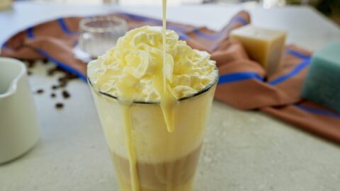 Pouring white chocolate coffee syrup over a latte macchiato.