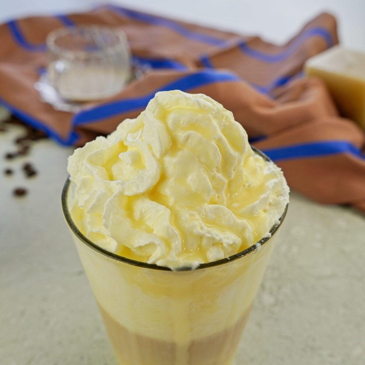 A cup of latte with whipped cream, layered coffee, and topped with white chocolate syrup.